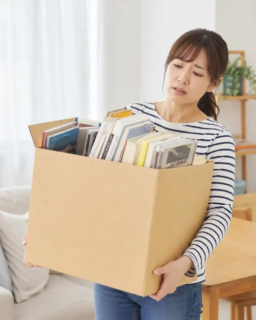 本やCDを詰めた重い段ボール箱を抱えて困っている女性